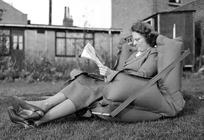 A Woman using an inflatable chair and reading a newspaper in the garden dated 1956