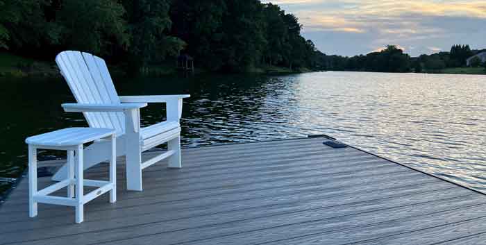 White Adirondack chair with a white side table combined on a floating deck on a lake.