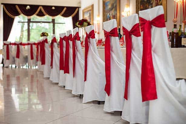 Elegantly decorated Banquet Chairs at a wedding reception hall with red ribbons on a marble floor